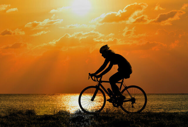 A woman rides her bike in the sunset along side the beach
