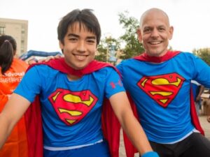 MRE employee posing with superhero cape with teenager at charity event